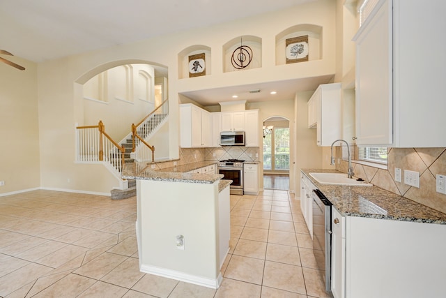 kitchen with appliances with stainless steel finishes, stone counters, light tile patterned floors, white cabinets, and sink