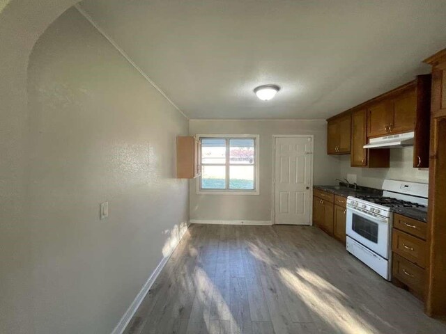 1507 Demaree Ln, Houston, TX 77029 - kitchen featuring white gas stove, under cabinet range hood, baseboards, dark countertops, and wood finished floors