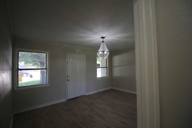 spare room with dark hardwood / wood-style flooring, a wealth of natural light, and an inviting chandelier