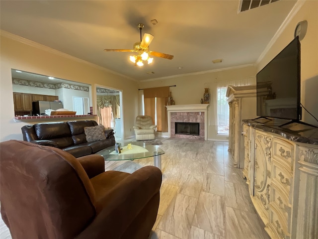 living room featuring crown molding, ceiling fan, and a tiled fireplace