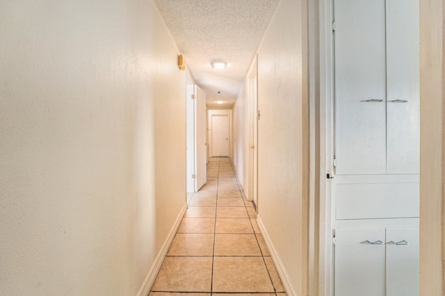 hallway with a textured ceiling and light tile patterned floors