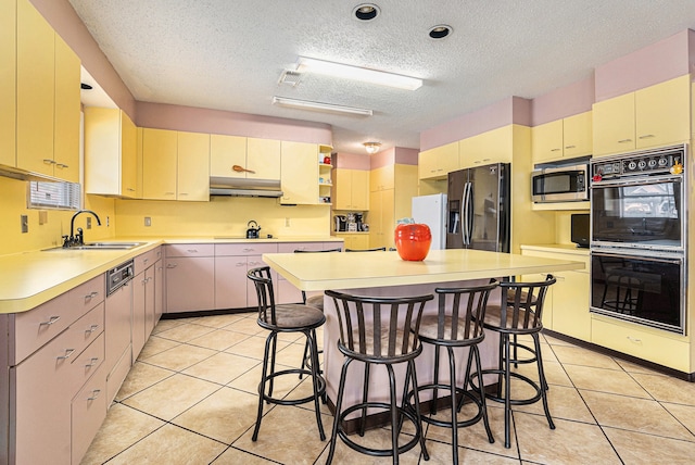 kitchen featuring a textured ceiling, black appliances, light tile patterned floors, a center island, and sink