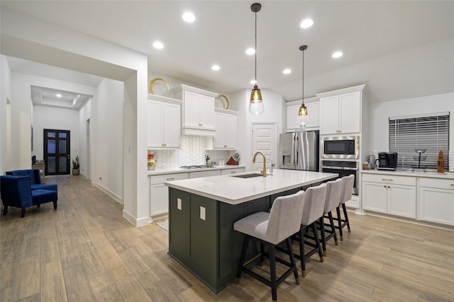 kitchen with light hardwood / wood-style floors, sink, appliances with stainless steel finishes, and a kitchen island with sink