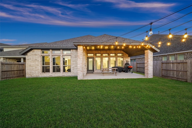 back house at dusk featuring a patio area and a yard