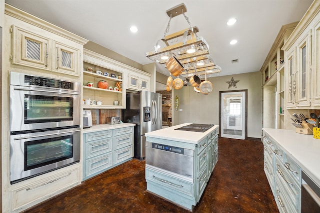 kitchen with appliances with stainless steel finishes, a kitchen island, cream cabinets, and hanging light fixtures