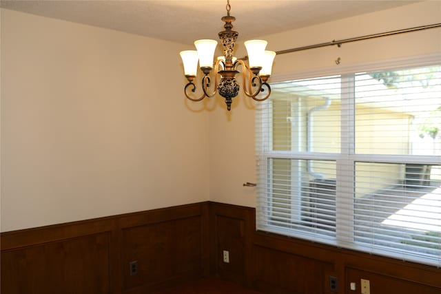 unfurnished room featuring wood walls and a notable chandelier