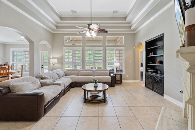 living area featuring built in shelves, a ceiling fan, light tile patterned floors, arched walkways, and a raised ceiling