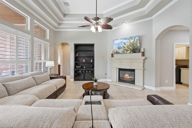 living room with visible vents, crown molding, a tray ceiling, light tile patterned floors, and arched walkways