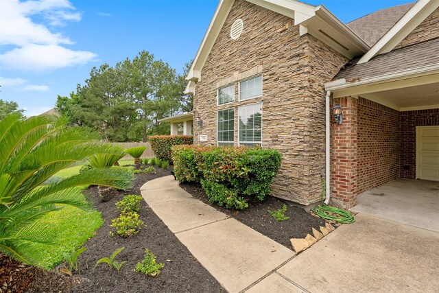 view of side of home featuring stone siding and a shingled roof