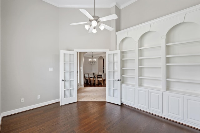 empty room featuring ornamental molding, ceiling fan with notable chandelier, wood finished floors, french doors, and baseboards