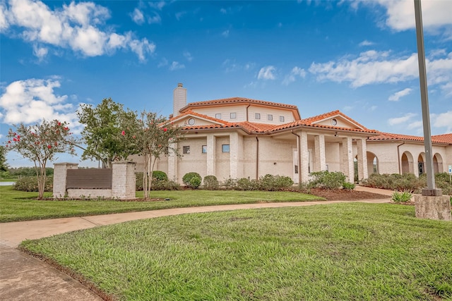 mediterranean / spanish home featuring a tile roof, a chimney, and a front lawn