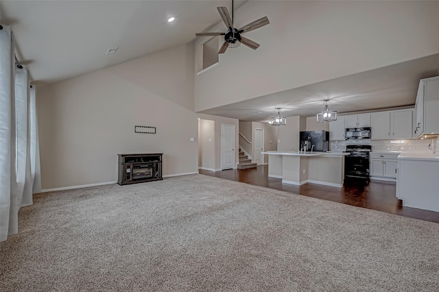 unfurnished living room with ceiling fan with notable chandelier, a towering ceiling, baseboards, stairway, and dark carpet