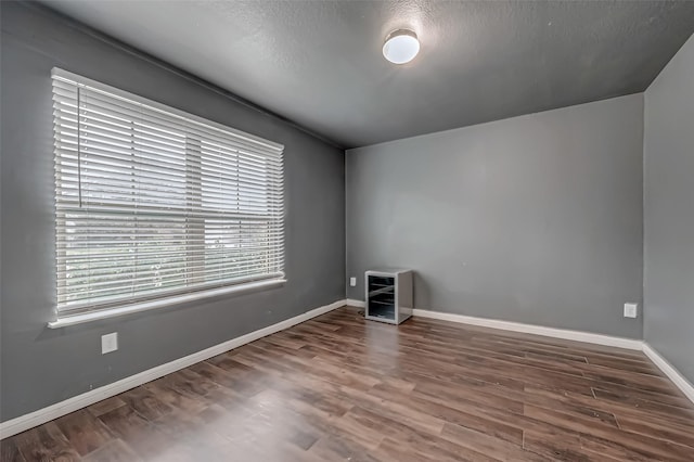 spare room with a textured ceiling, wood finished floors, and baseboards