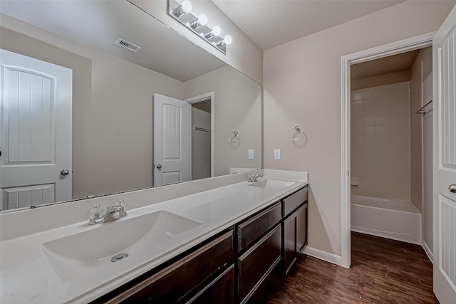 full bathroom with double vanity, visible vents, a sink, and wood finished floors