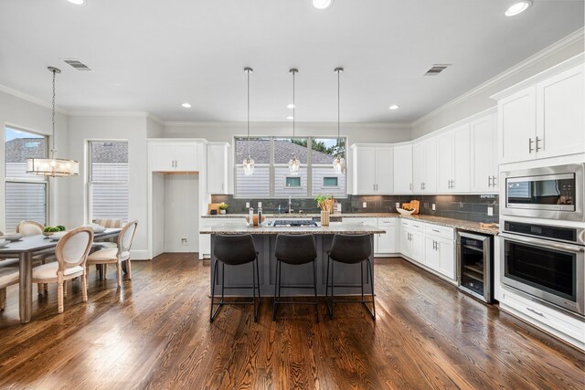 kitchen with wine cooler, a kitchen island, white cabinetry, light stone countertops, and stainless steel appliances