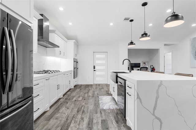 kitchen featuring light wood-type flooring, stainless steel appliances, white cabinetry, wall chimney exhaust hood, and pendant lighting