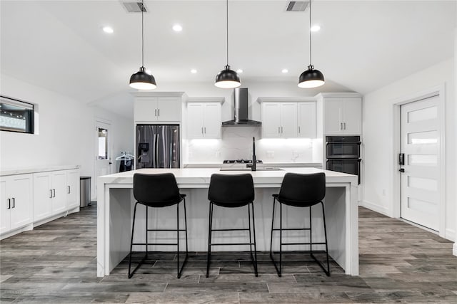 kitchen with vaulted ceiling, dark hardwood / wood-style flooring, wall chimney range hood, stainless steel fridge, and a center island with sink