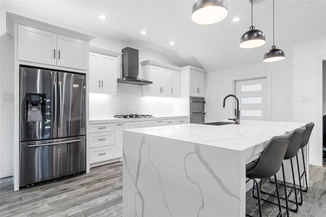 kitchen featuring a center island with sink, stainless steel appliances, wall chimney exhaust hood, and white cabinetry