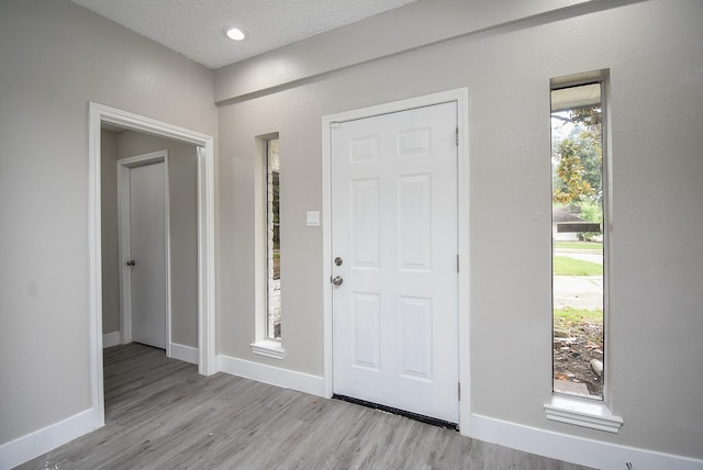 foyer entrance featuring baseboards, a textured ceiling, and light wood finished floors