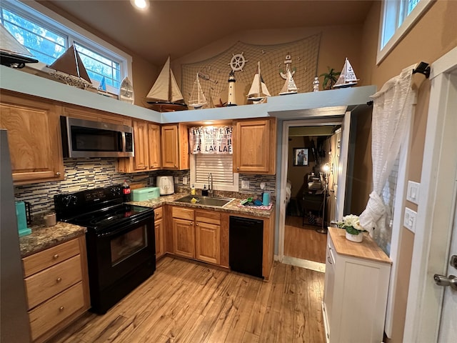 kitchen with black appliances, sink, a towering ceiling, stone countertops, and light hardwood / wood-style floors