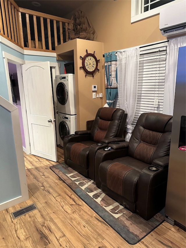 living room featuring stacked washer and clothes dryer, a high ceiling, a wall unit AC, and light hardwood / wood-style floors