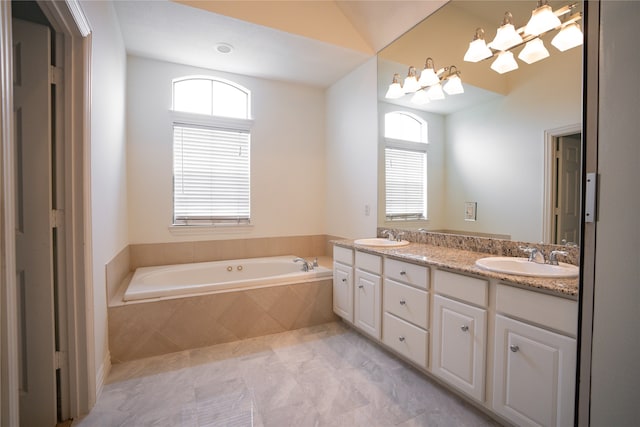 bathroom featuring lofted ceiling, vanity, a chandelier, and tiled bath