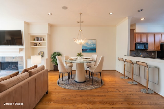 dining space with a fireplace, ornamental molding, a chandelier, and light wood-type flooring