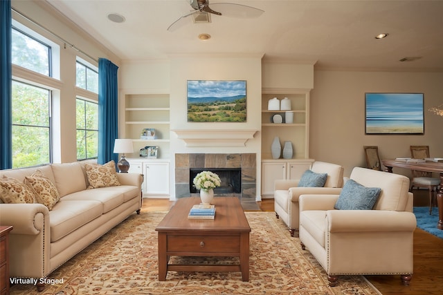 living room with light wood-type flooring, a fireplace, ceiling fan, crown molding, and built in shelves