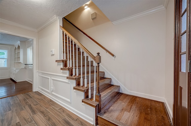 stairs with a textured ceiling, ornamental molding, and wood-type flooring