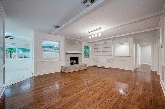 unfurnished living room with a textured ceiling, built in features, a large fireplace, hardwood / wood-style flooring, and ceiling fan