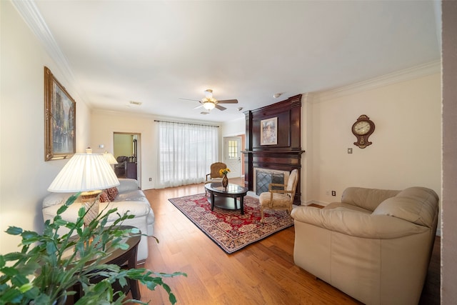 living room featuring ornamental molding, a large fireplace, ceiling fan, and hardwood / wood-style floors