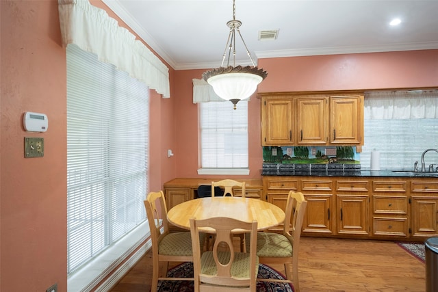 dining room featuring sink, light wood-type flooring, plenty of natural light, and ornamental molding