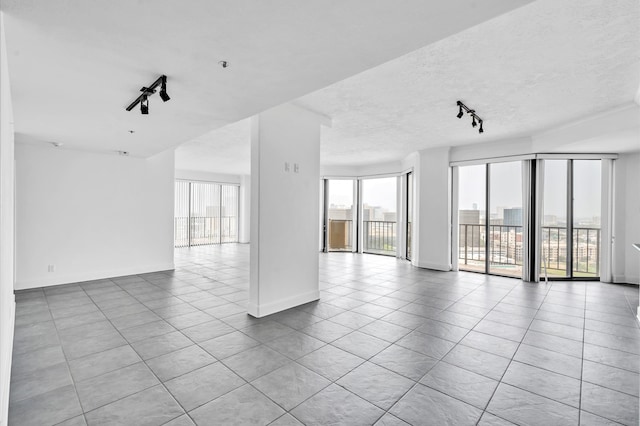 tiled spare room with a textured ceiling, a wealth of natural light, and rail lighting