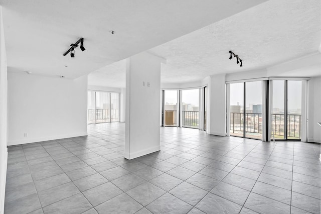 tiled spare room featuring baseboards, track lighting, and a textured ceiling