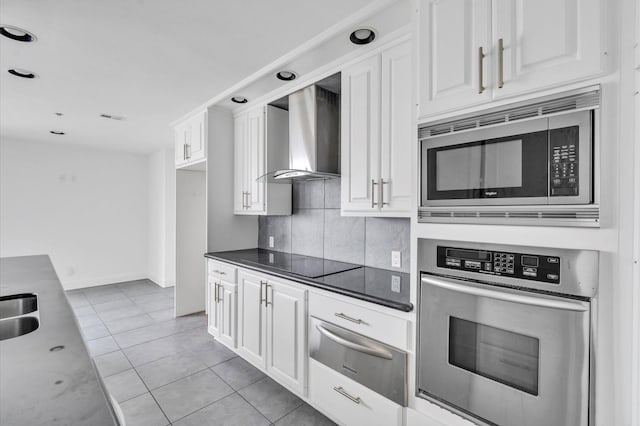 kitchen featuring wall chimney range hood, appliances with stainless steel finishes, white cabinetry, a warming drawer, and backsplash