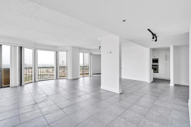 unfurnished living room featuring baseboards, rail lighting, and a textured ceiling