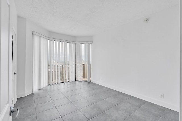 empty room featuring tile patterned flooring, baseboards, and a textured ceiling