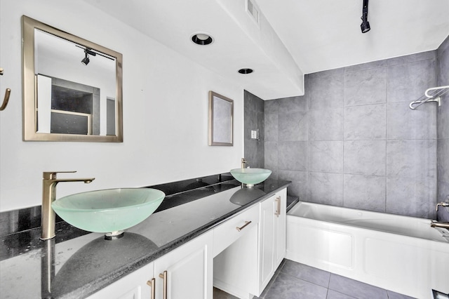 full bath featuring tile patterned floors, a sink, double vanity, and a tub to relax in