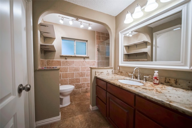 bathroom featuring vanity, toilet, tile walls, and a textured ceiling