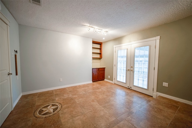 tiled empty room with french doors, rail lighting, and a textured ceiling