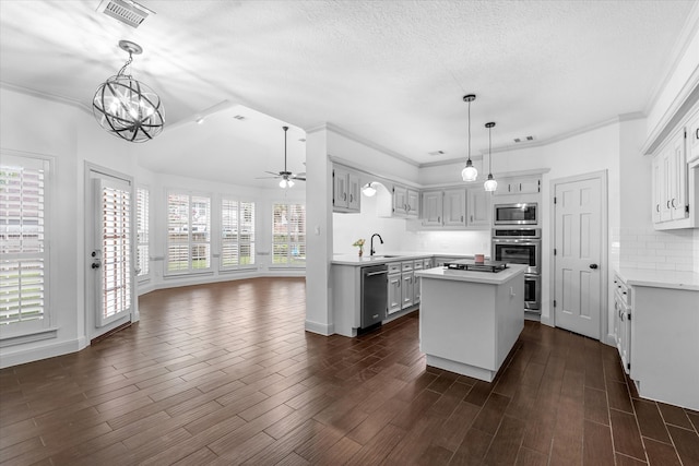 kitchen with appliances with stainless steel finishes, ceiling fan with notable chandelier, a kitchen island, and dark hardwood / wood-style flooring