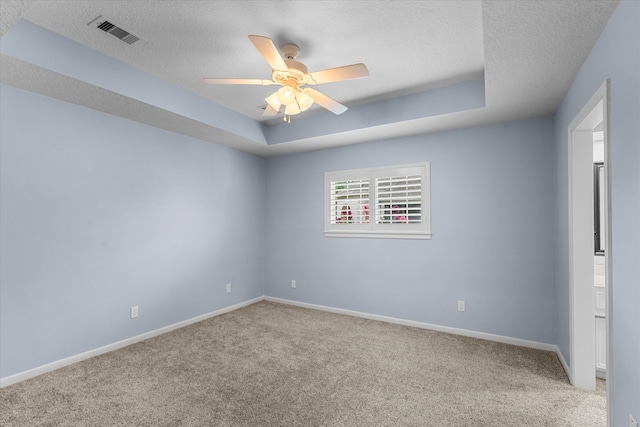 carpeted spare room featuring a textured ceiling, ceiling fan, and a tray ceiling