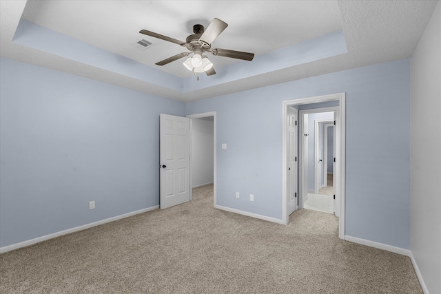 unfurnished bedroom with a tray ceiling, a textured ceiling, light carpet, and ceiling fan