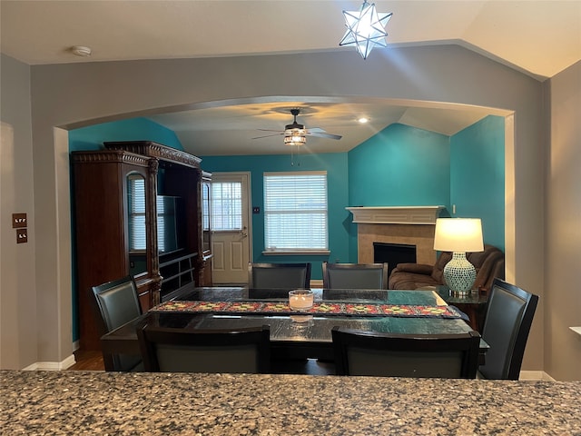 dining space with a fireplace, ceiling fan, and vaulted ceiling