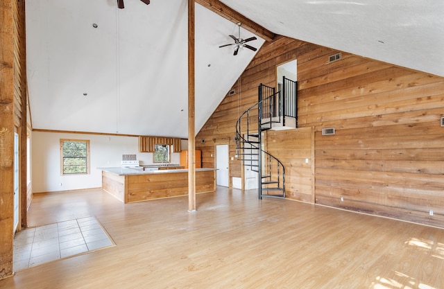 unfurnished living room with light hardwood / wood-style flooring, ceiling fan, wood walls, and high vaulted ceiling