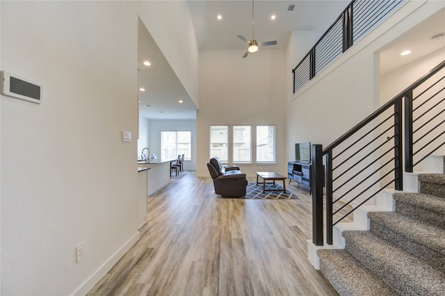 foyer with ceiling fan, sink, light wood-type flooring, and a high ceiling