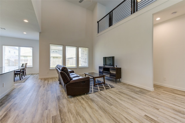 living room featuring light hardwood / wood-style flooring, a high ceiling, and a healthy amount of sunlight