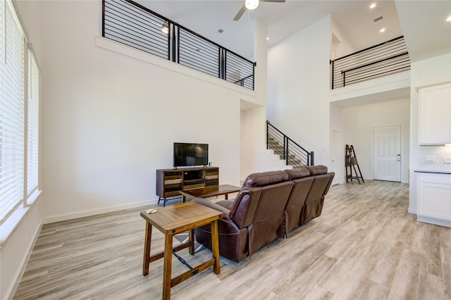 living room featuring ceiling fan, a towering ceiling, and light wood-type flooring