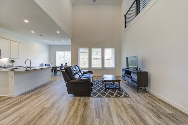 living room with light hardwood / wood-style flooring, sink, and a towering ceiling