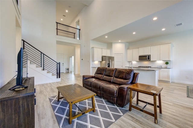 living room featuring light wood-type flooring, sink, and a towering ceiling